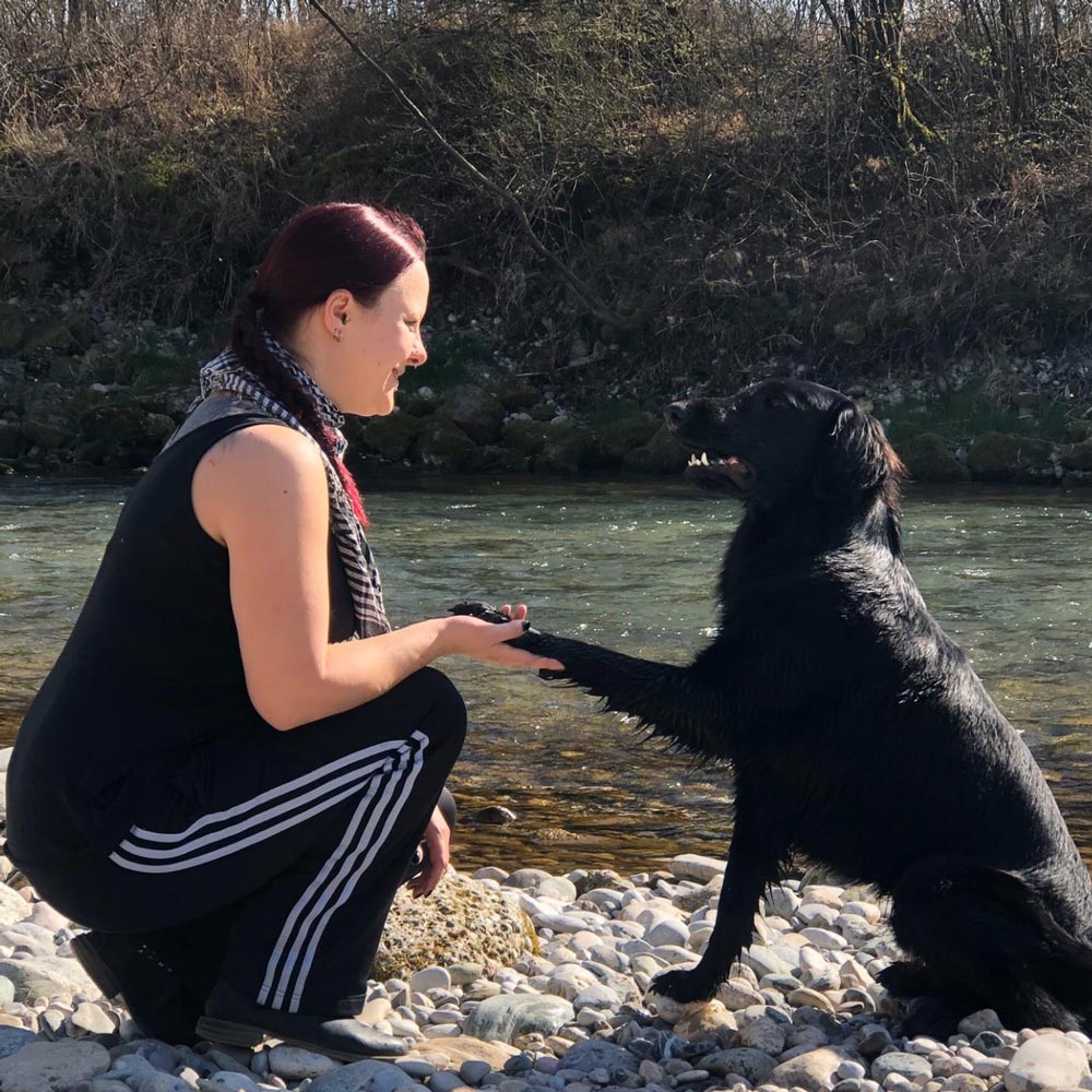 Schwarzer Hund gibt Hundetrainerin vor einer Brücke an der Alz die Pfote beim Bindungstraining